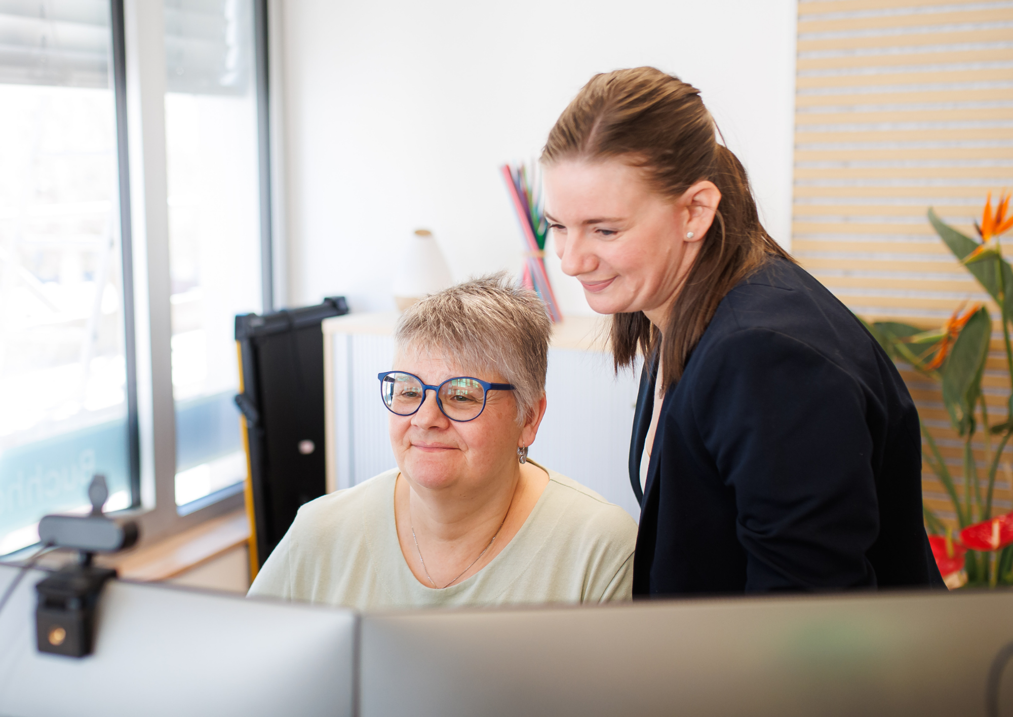 Zwei Frauen, Evelyn Paul und Denise Paul, stehen in ihrem Büro und schauen auf einen Bildschirm.